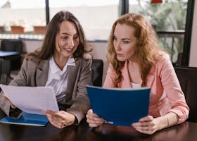Two businesswomen reviewing documents together in an office setting, emphasizing teamwork and cooperation.