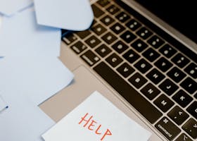 A laptop covered with sticky notes and a prominent "Help" sign, conveying urgency.